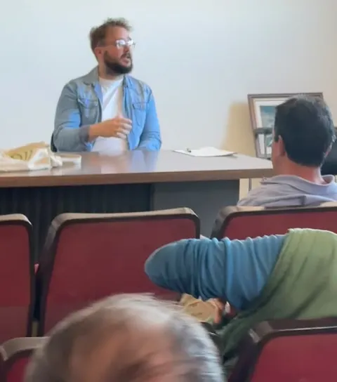 Oriol hablando ante el público en una sala de sillas rojas